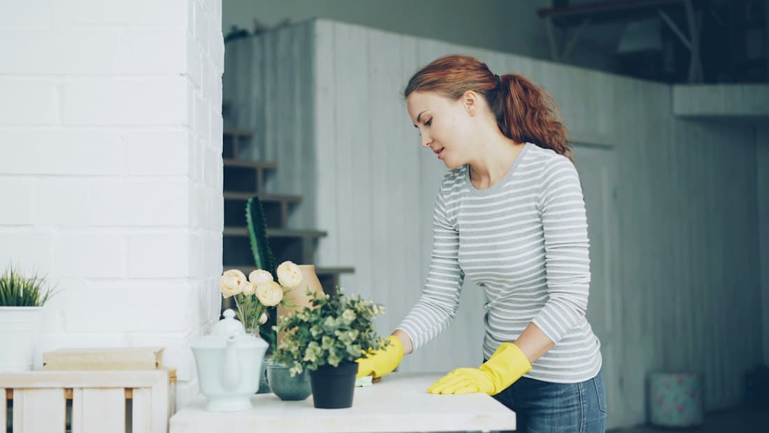 A woman in yellow cleaning gloves wiping a table